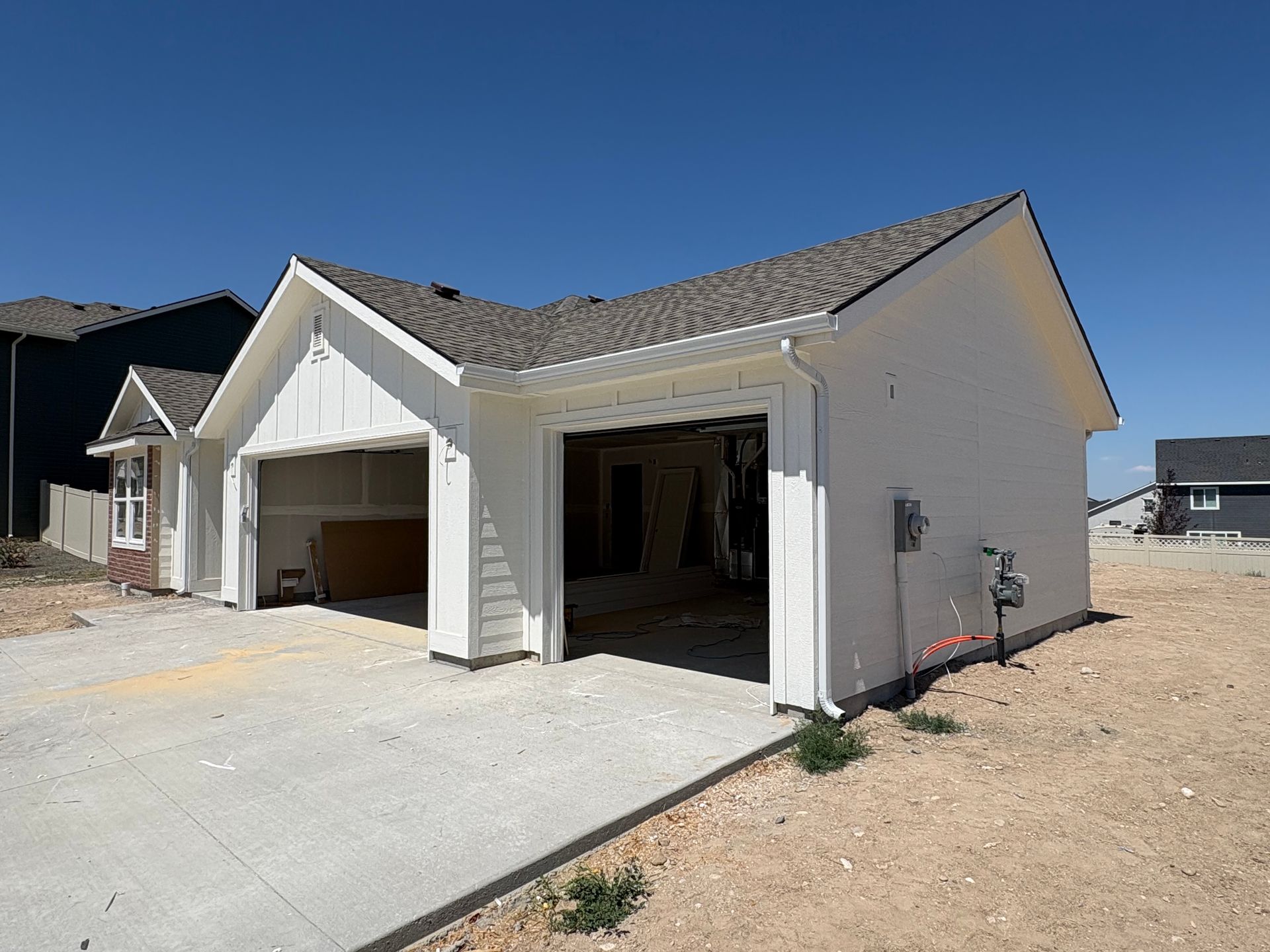 Newly constructed white house with attached two-car garage, concrete driveway, and brown roof under a blue sky.