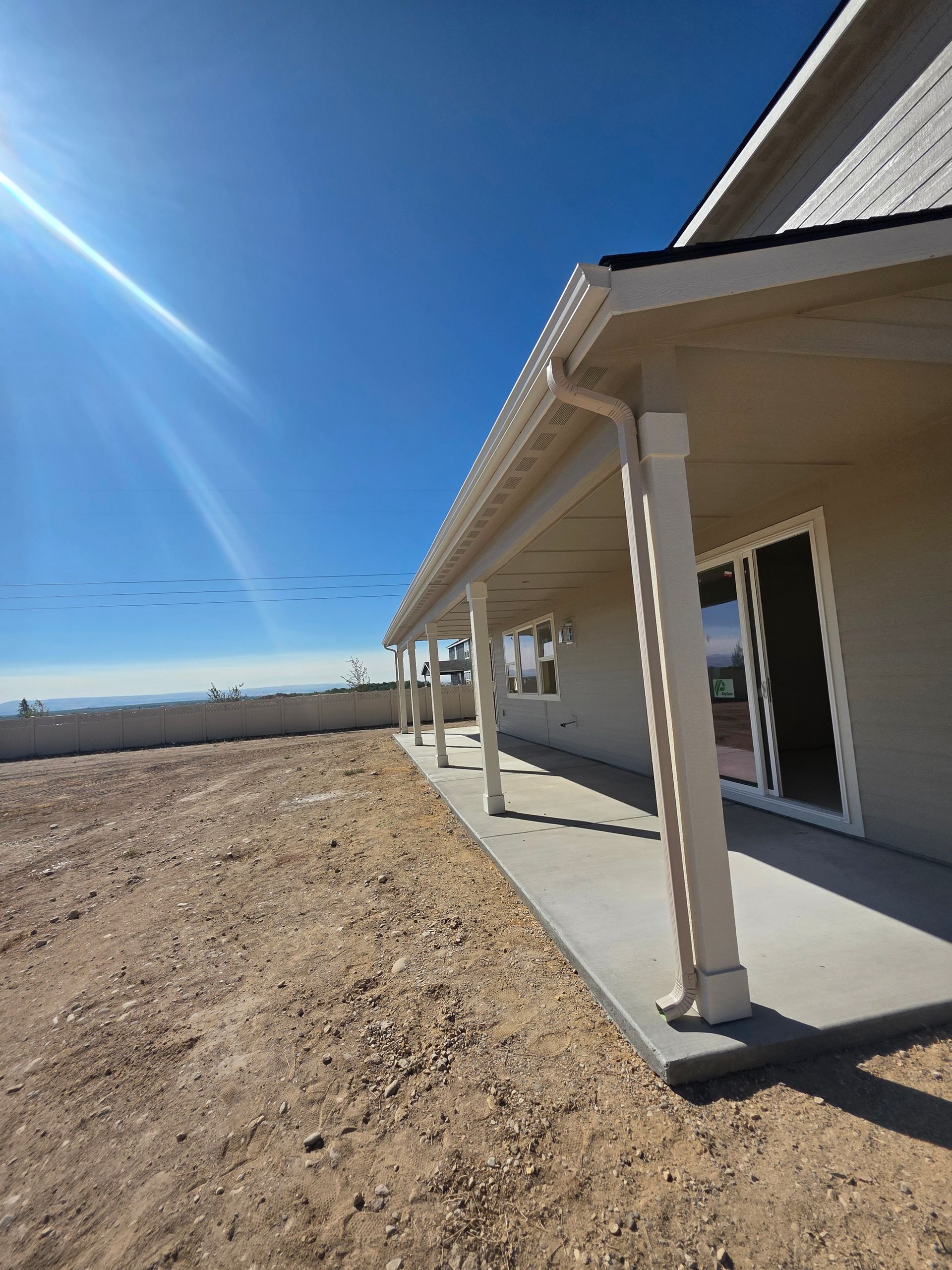 Beige house with porch, concrete patio, and a clear blue sky.