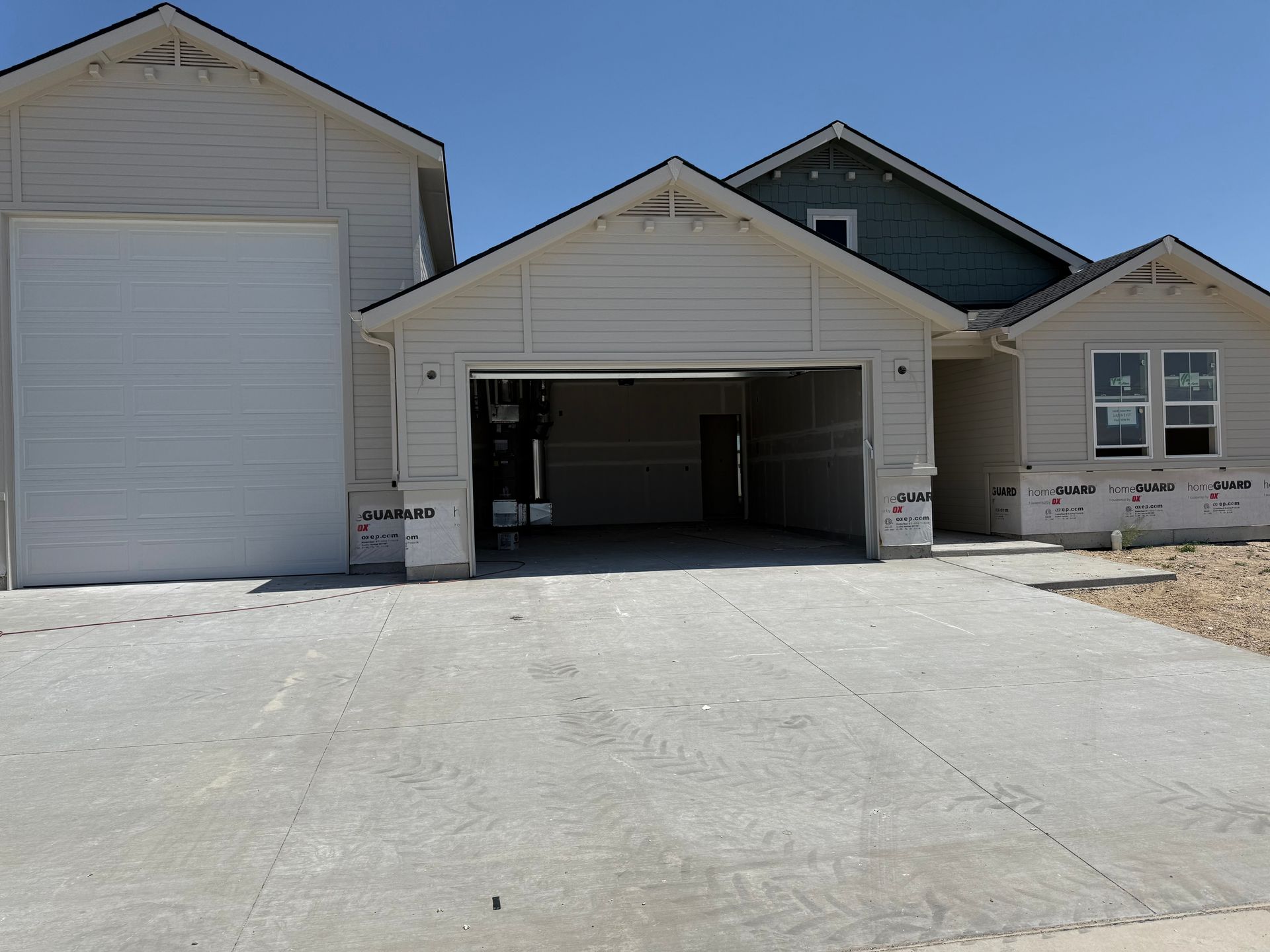 A house under construction with a concrete driveway and an open garage, on a sunny day.