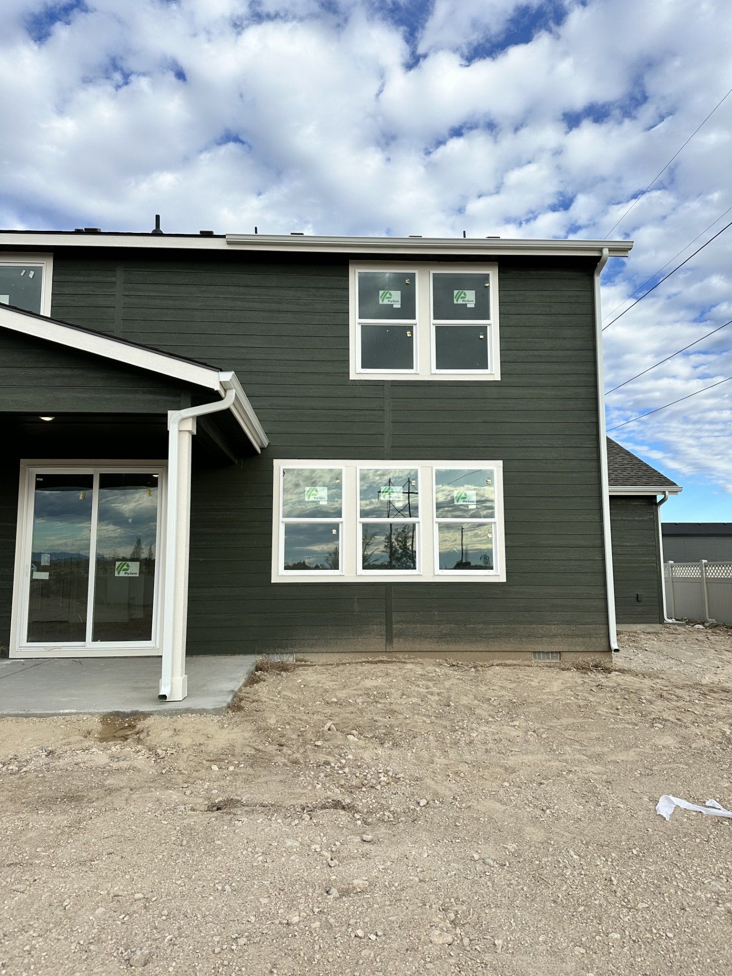 Dark green house exterior with white-framed windows against a cloudy sky.