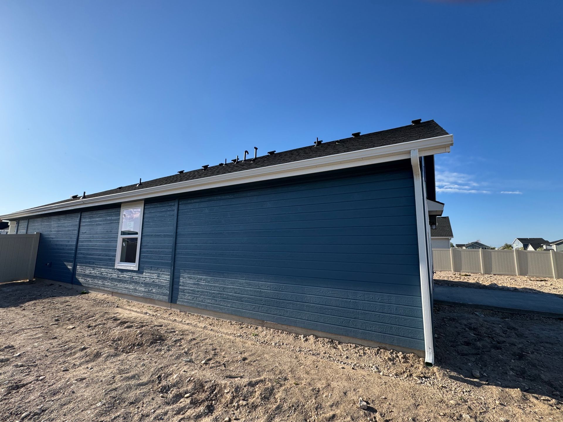 Blue-sided building under construction against a clear blue sky. White gutter and a single window are visible.
