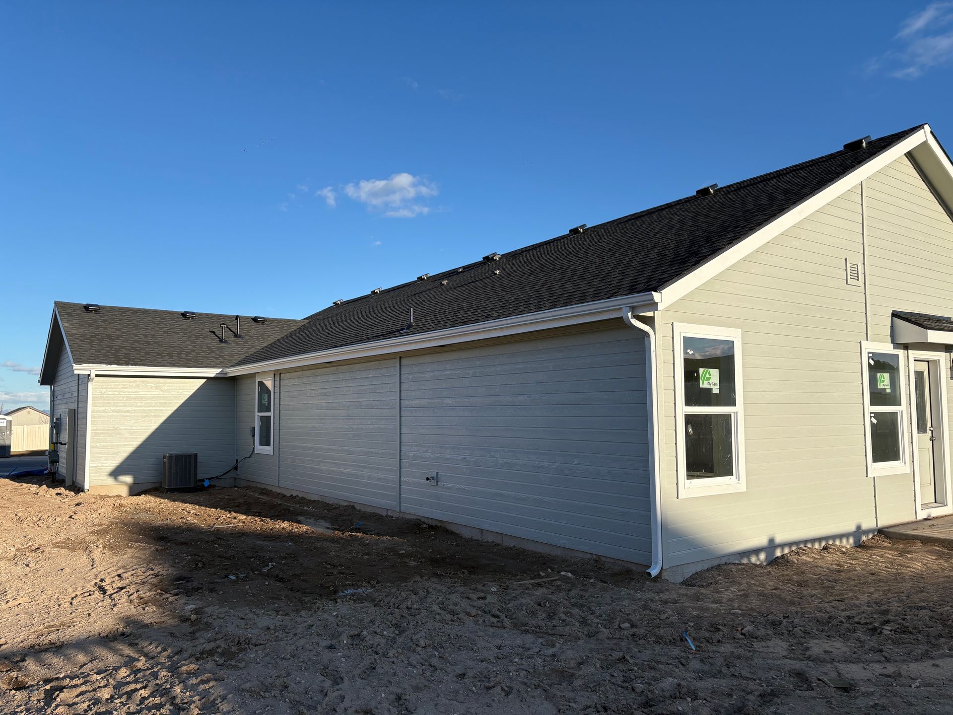 Light gray house exterior with black roof, white trim, and two windows; dirt in front.