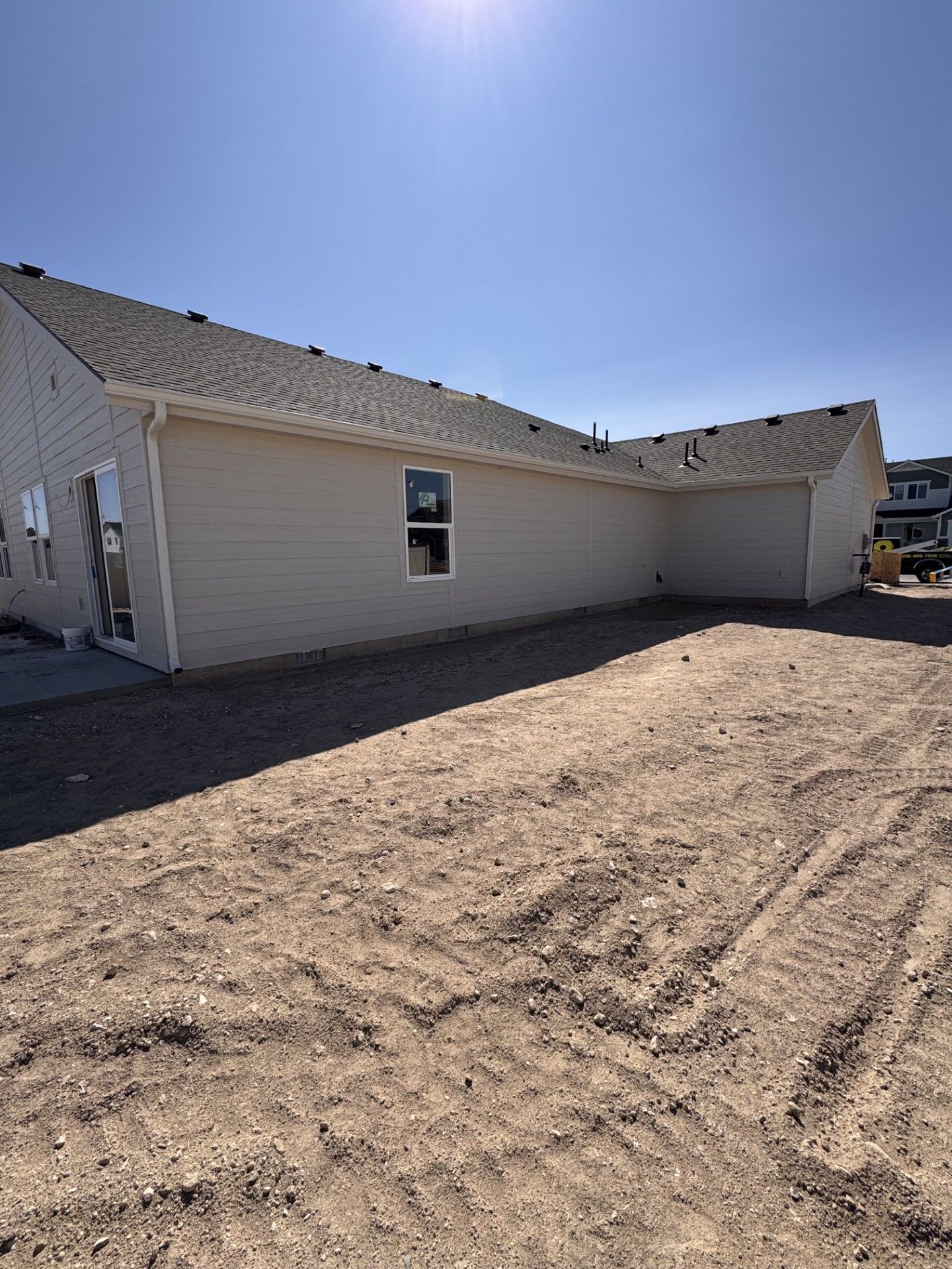 Exterior view of a beige house under construction with a clear blue sky and dirt ground.