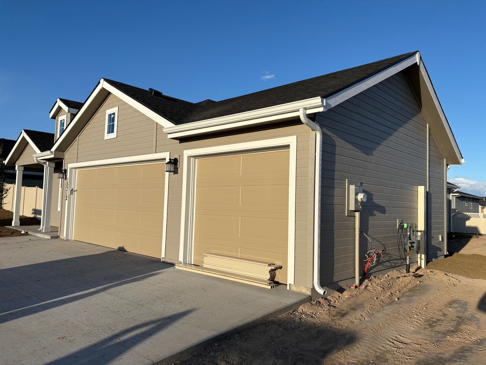 Tan garage doors on a gray house with a black roof and blue sky.