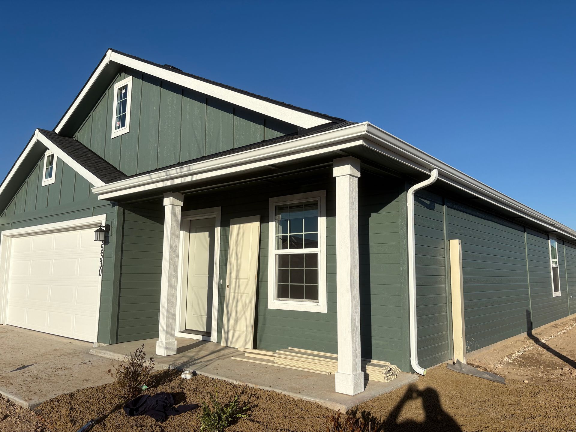Green house with white trim, garage, porch with pillars. Clear blue sky.
