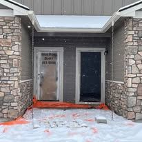 Exterior of building with two doors, one frosted, and a snow-covered ground with orange barrier.