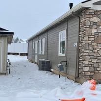 Snowy scene with a house and air conditioner.