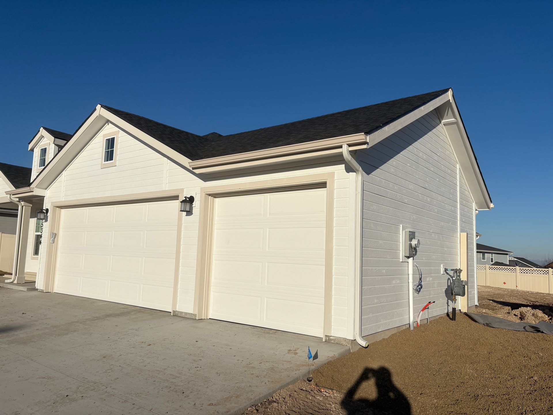 White two-car garage with cream trim and dark roof under a blue sky.