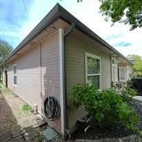Corner view of a house with light siding and an attached gutter system; sunny outdoors.