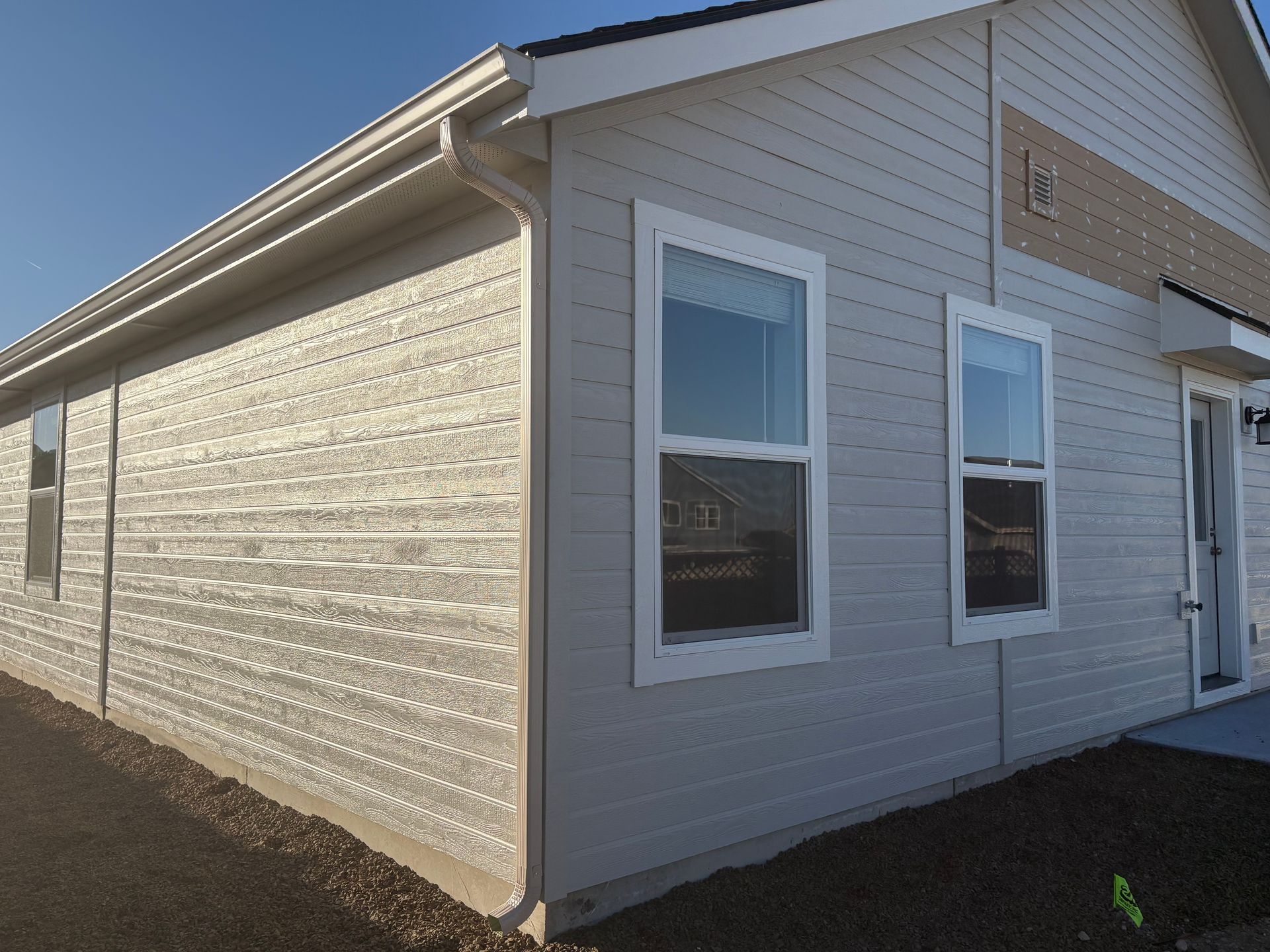 Light gray building with white-framed windows, gutters, and siding; sunny day.