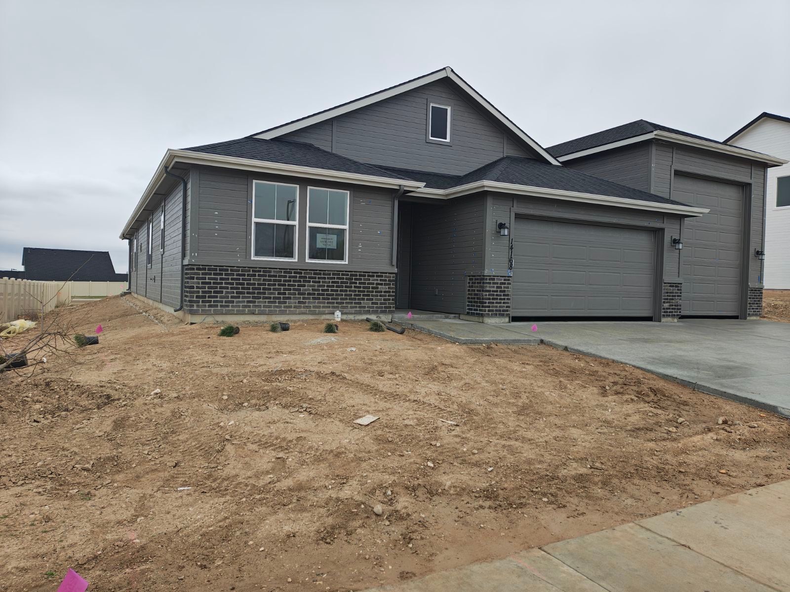 Gray house under construction, with a garage and bare earth yard.