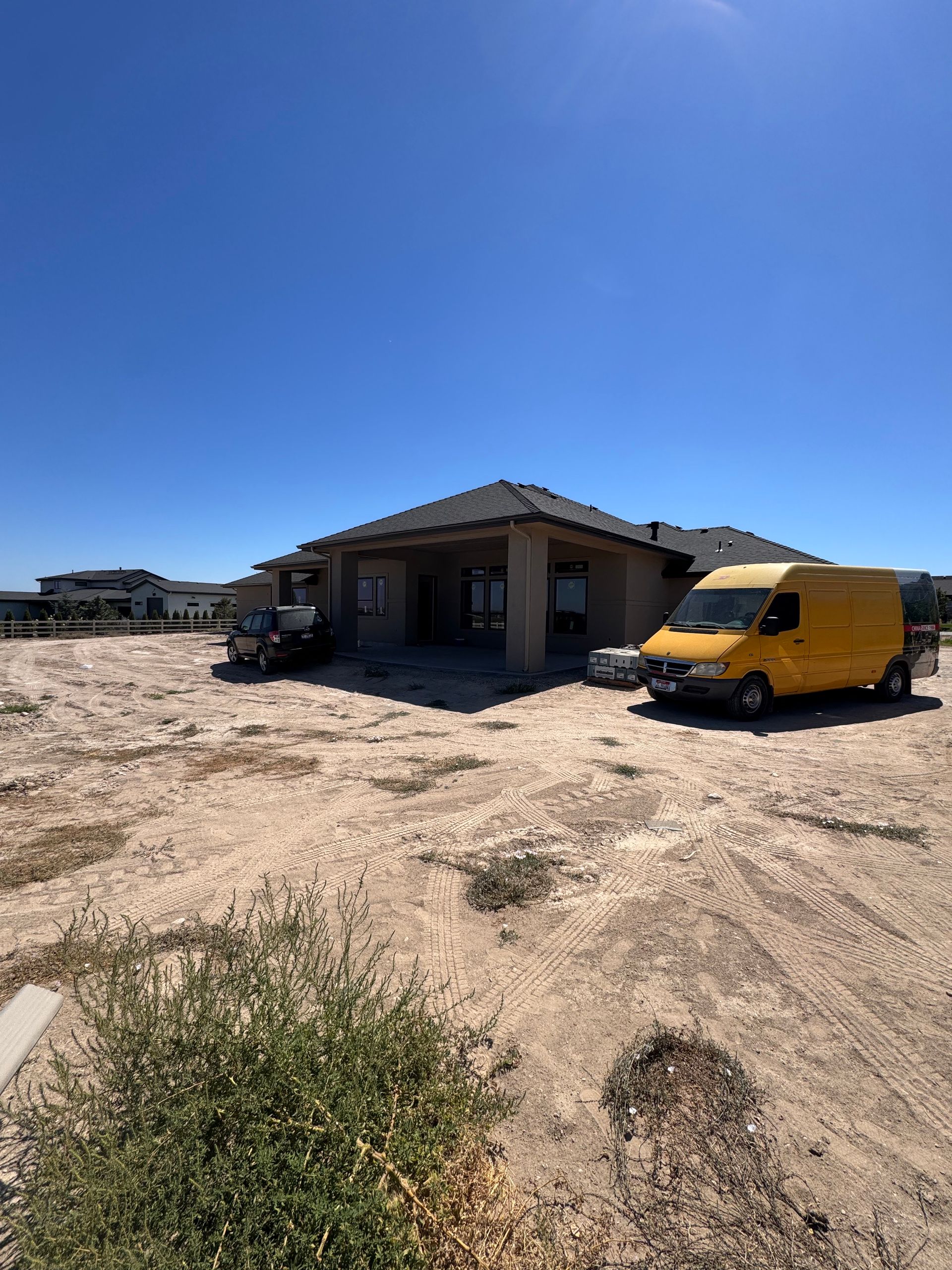 Construction site: single-story beige house under a clear blue sky, with yellow van parked nearby.