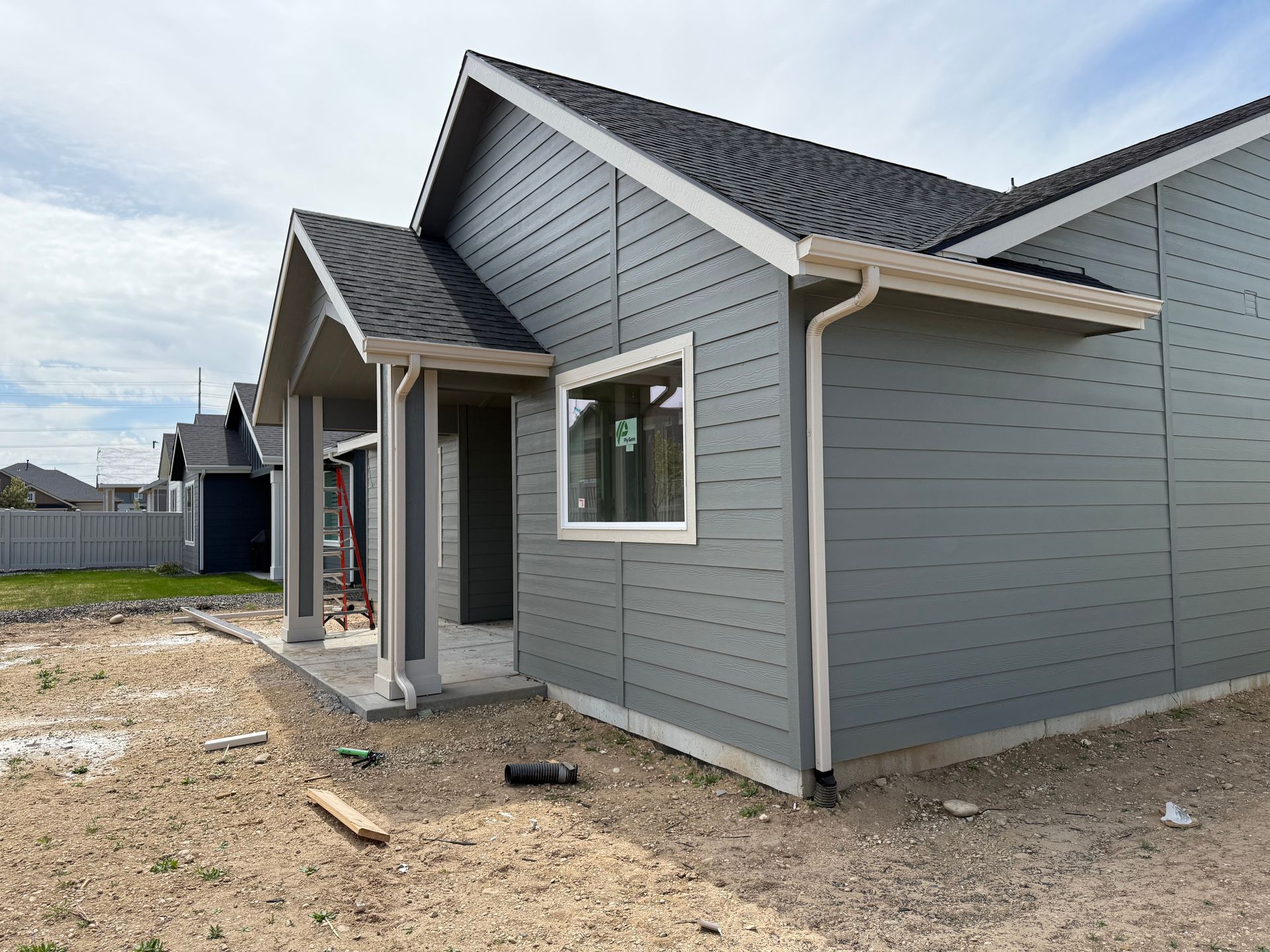 Gray house under construction, white window frame, black roof, beige soil.