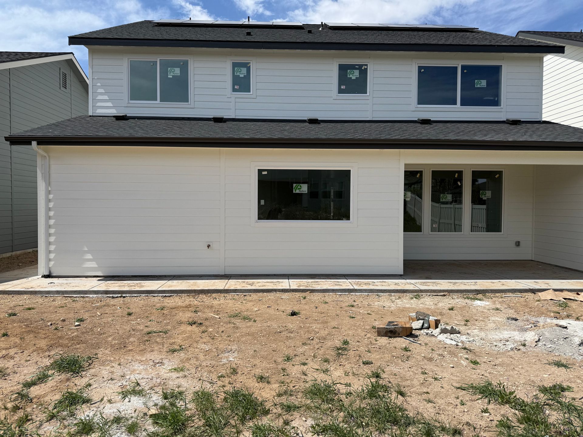 Rear view of a two-story house with white siding and black roof; a bare yard in front.
