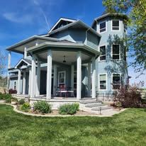 Light blue house with a covered front porch and tower under a blue sky.