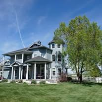 Blue-gray house with white columns, a tower, and green lawn, under a blue sky with a tree.