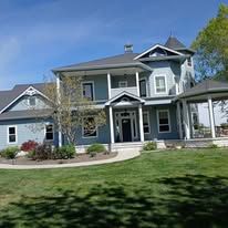 Blue two-story house with columns and a porch on a sunny day.