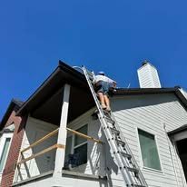 Person on a ladder repairing a roof. House exterior, blue sky.
