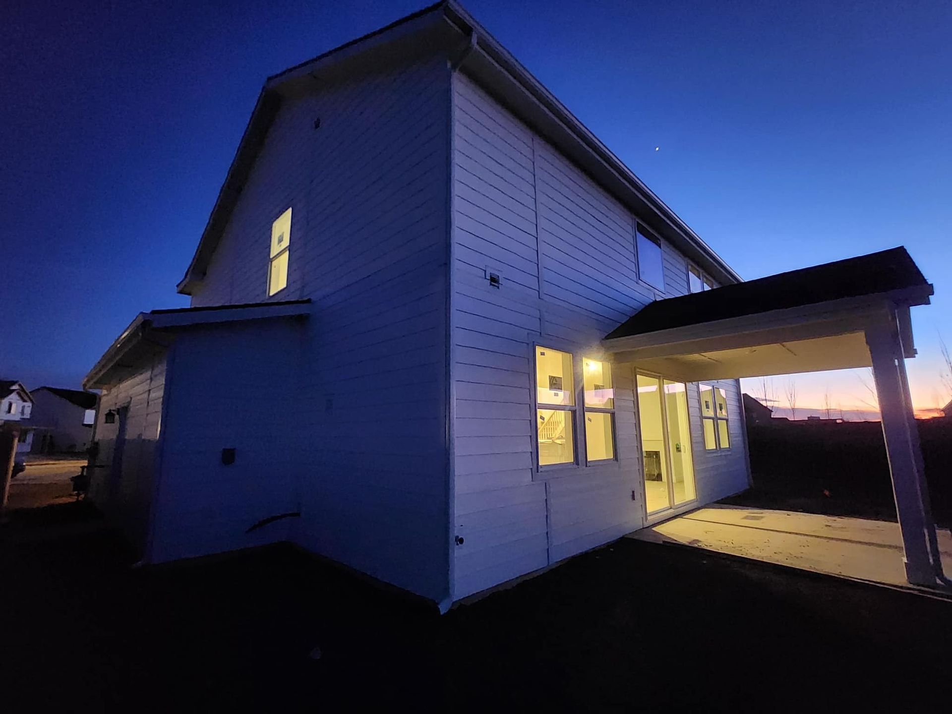 White two-story house at dusk, lit interior, porch, dark blue sky.