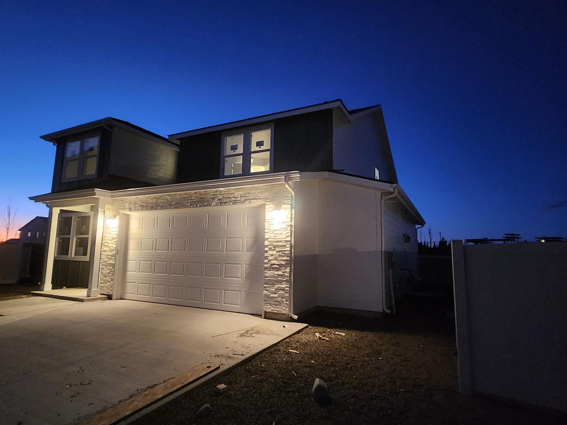 A two-story house at dusk with garage, lit exterior, and blue sky.