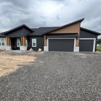 Modern home with dark exterior, wood accents, and gray gravel driveway.