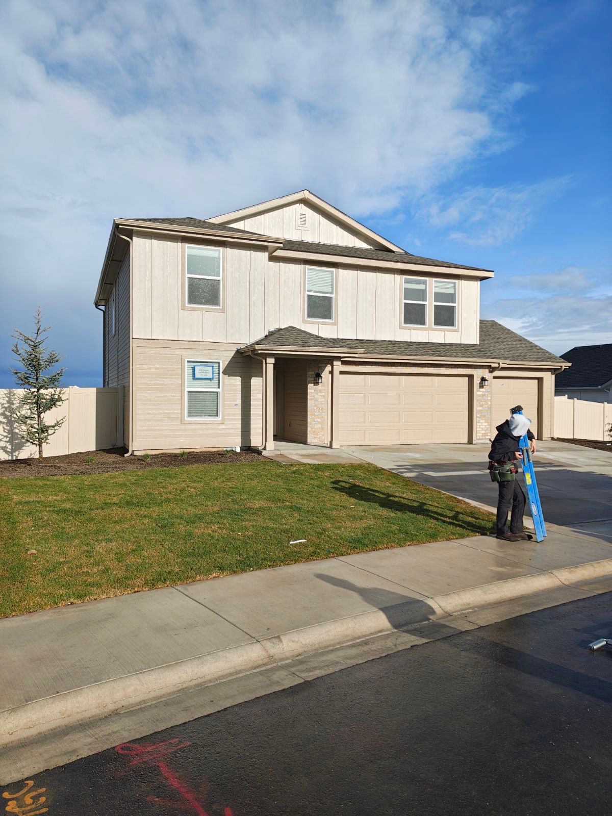 Two-story beige house with a two-car garage. People stand in front, and green lawn. Cloudy sky.