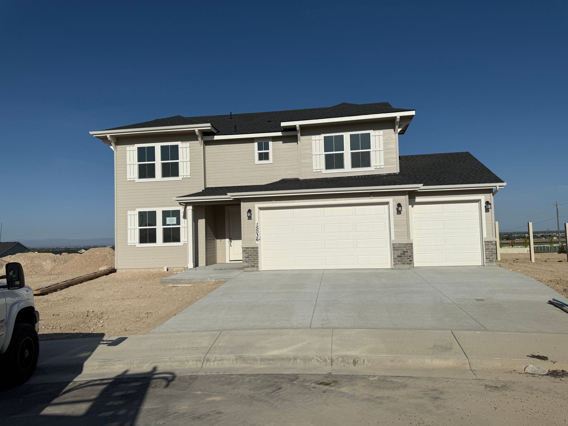 Two-story beige house with white trim, three-car garage, concrete driveway, under construction, blue sky.