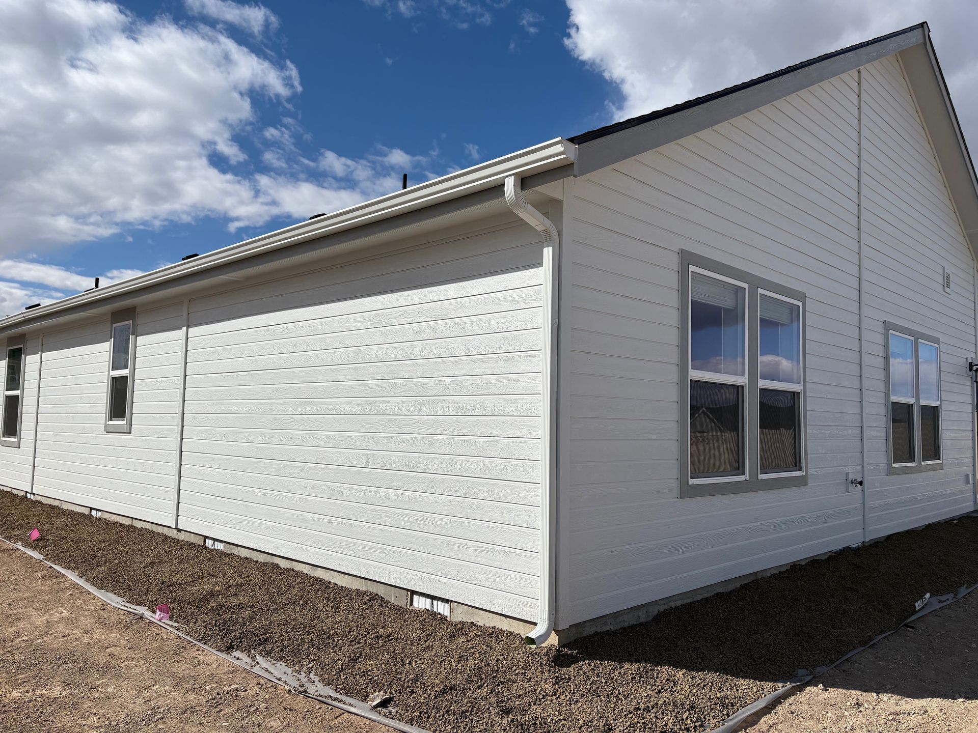 White house exterior with windows, gray trim, and guttering under a blue sky.