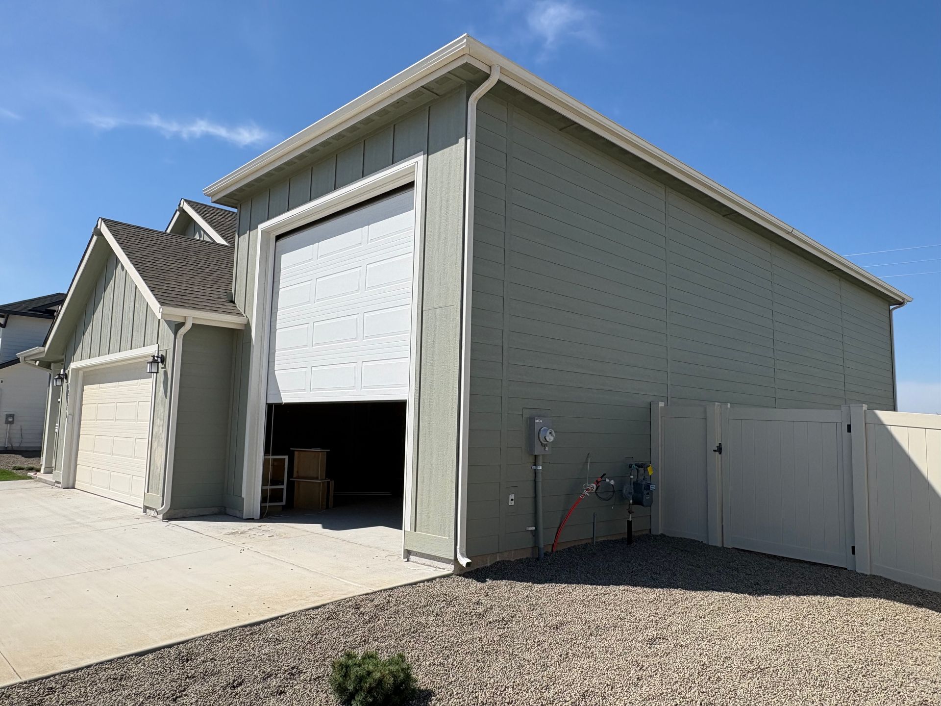 Garage exterior with an open overhead door, sage green siding, and a concrete driveway.