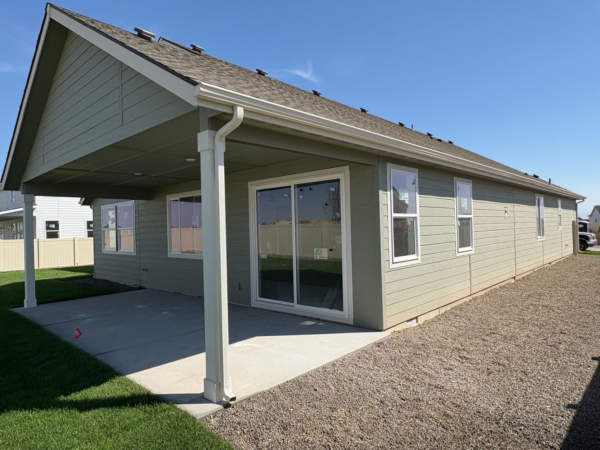 Back exterior of a house with a covered patio, beige siding, and gravel landscaping.