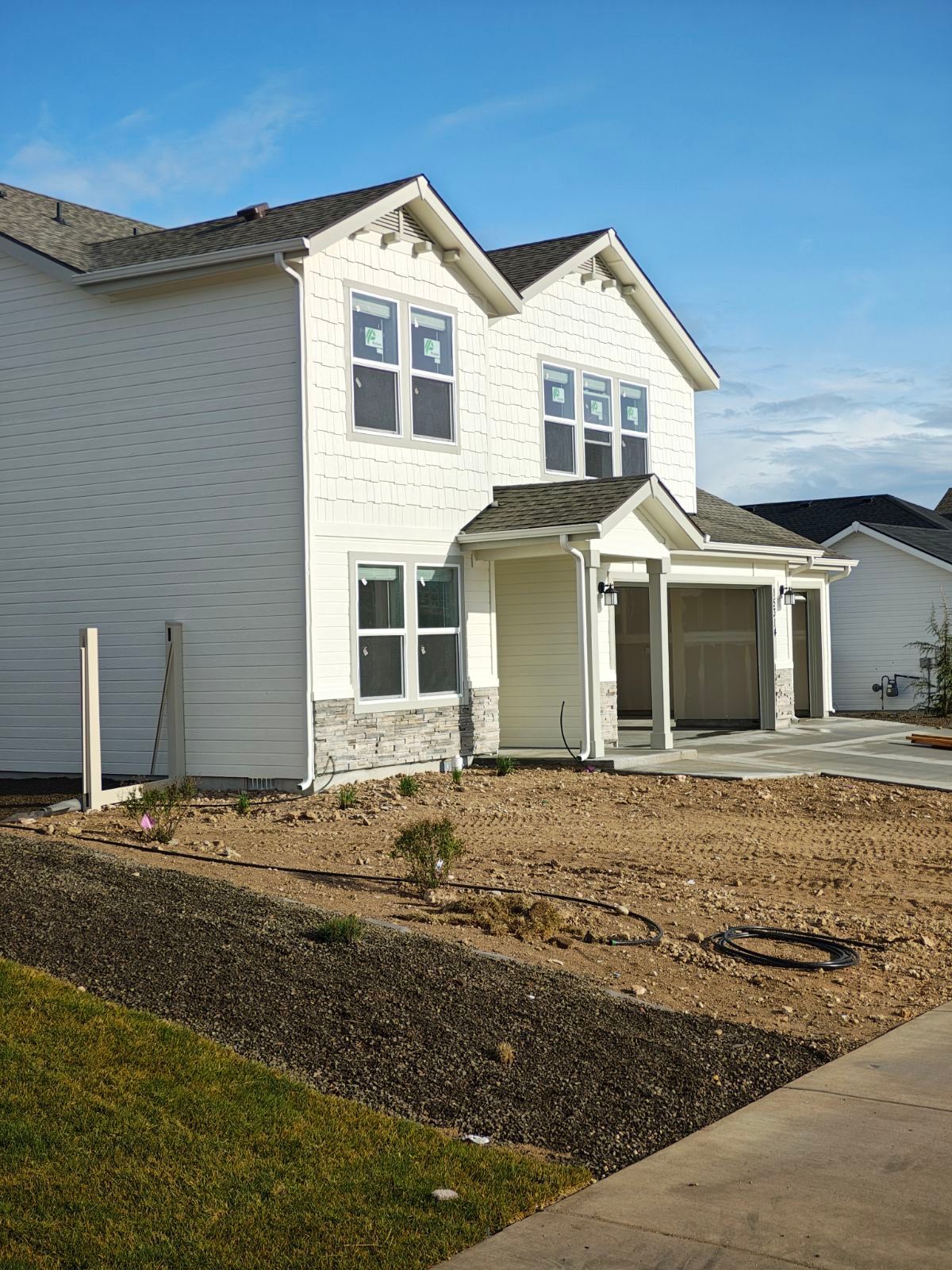 New two-story house under construction with white siding, stone accents, and unfinished landscaping.