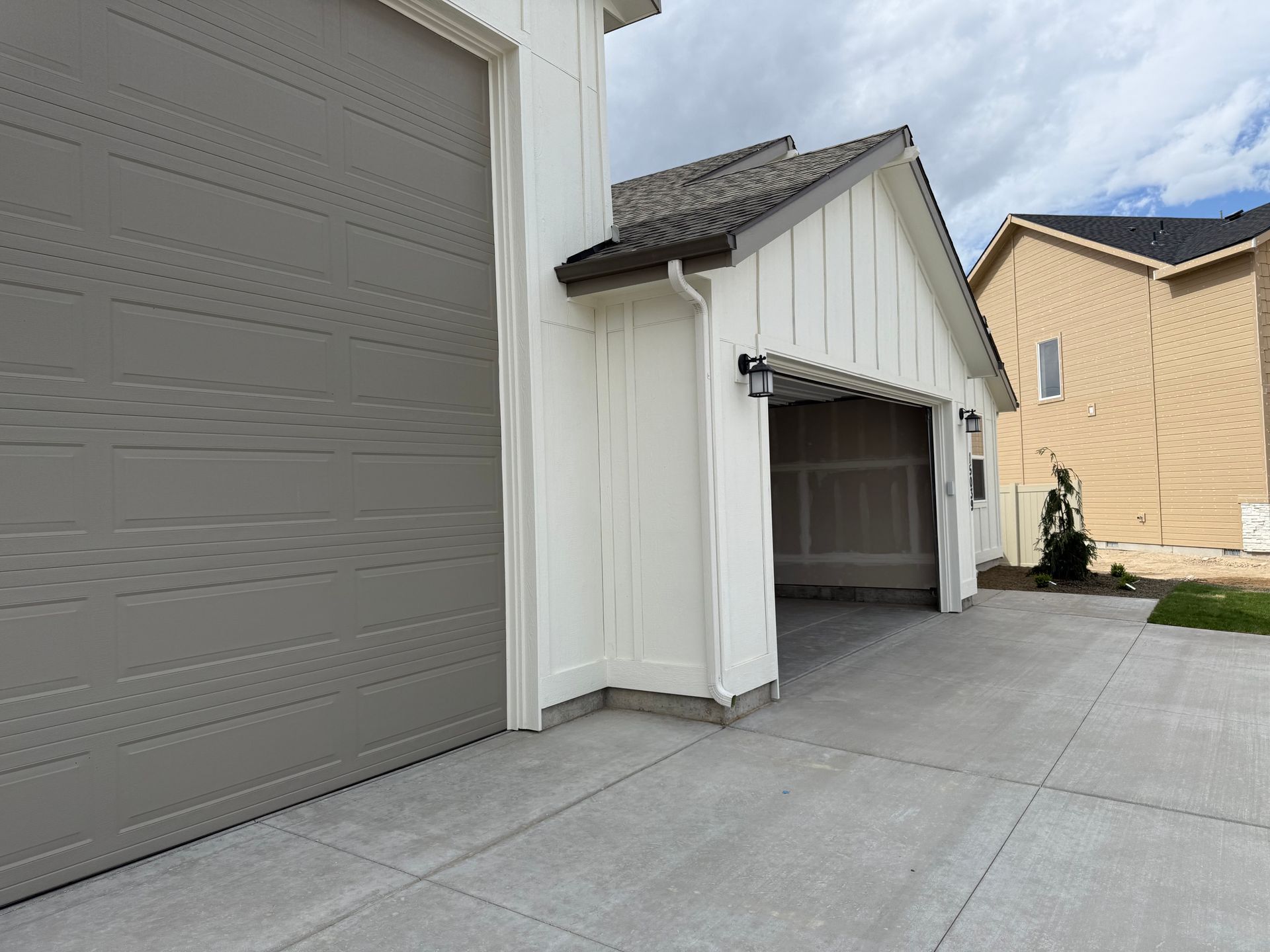 Exterior view of a house with a gray garage door and a white carport. The driveway is concrete.