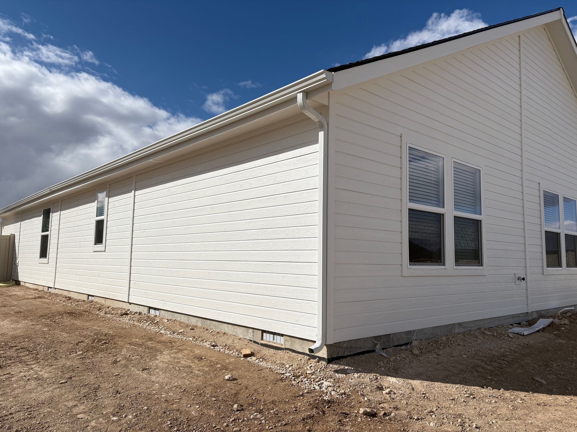 White house exterior with horizontal siding, windows, and gutter against a cloudy sky.