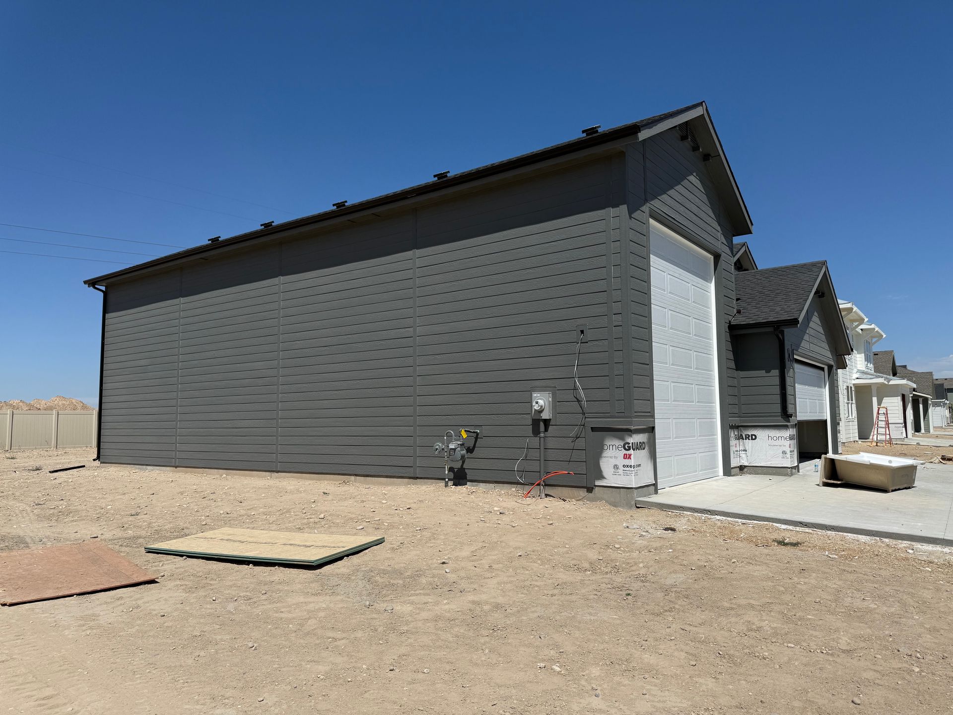 Gray-sided building under construction, blue sky. Gravel and concrete in foreground.