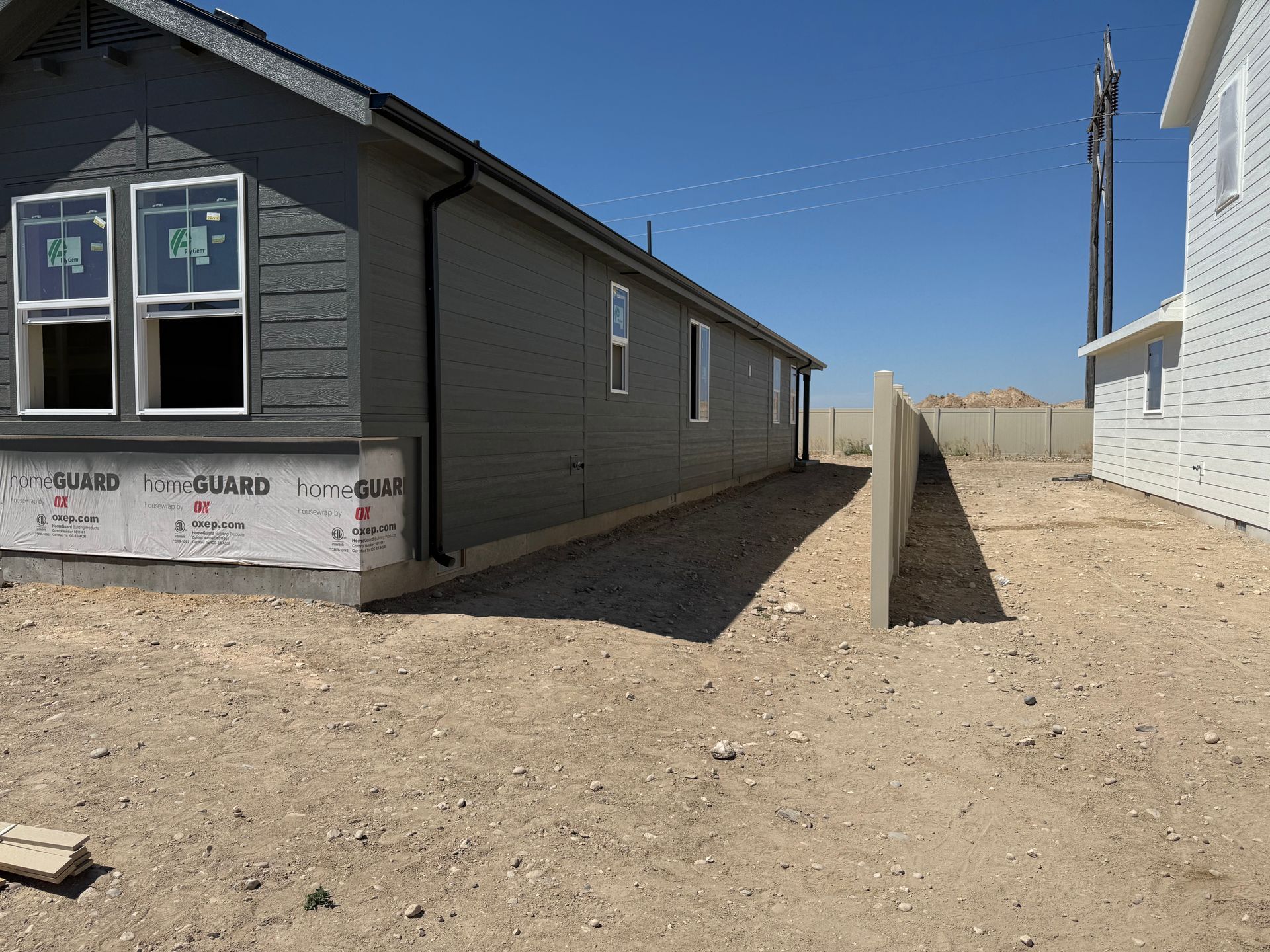 Side view of a gray house under construction with a gravel walkway and a concrete wall.