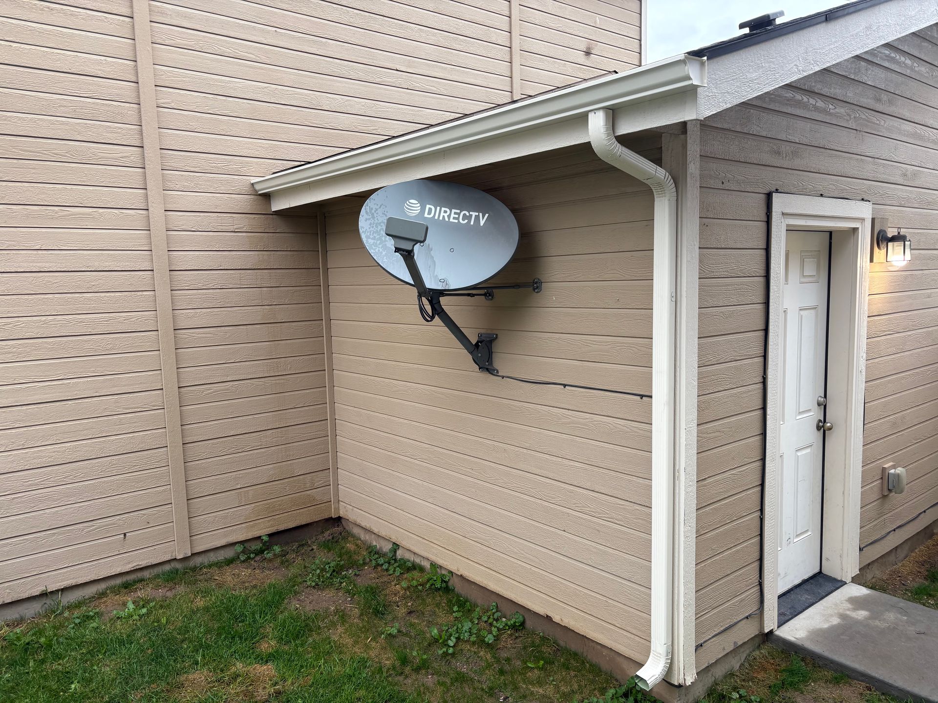 A satellite dish mounted on a beige building exterior next to a white door.