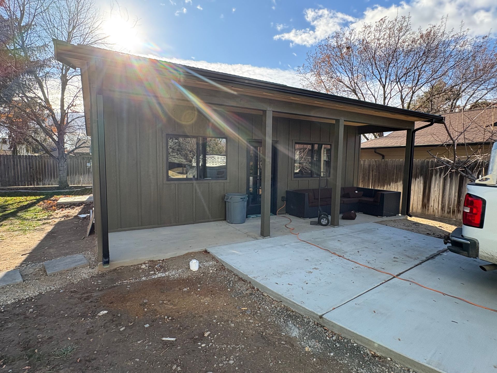 Gray building with covered porch and concrete driveway; bright sunlight.