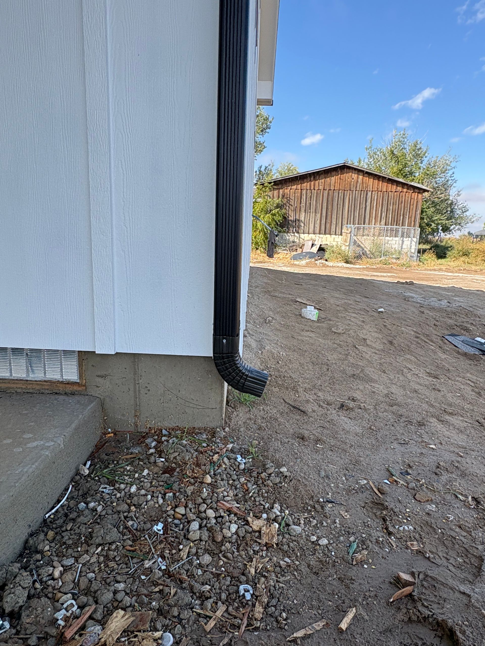 Black gutter on a white building wall with a concrete foundation on a gravelly ground.