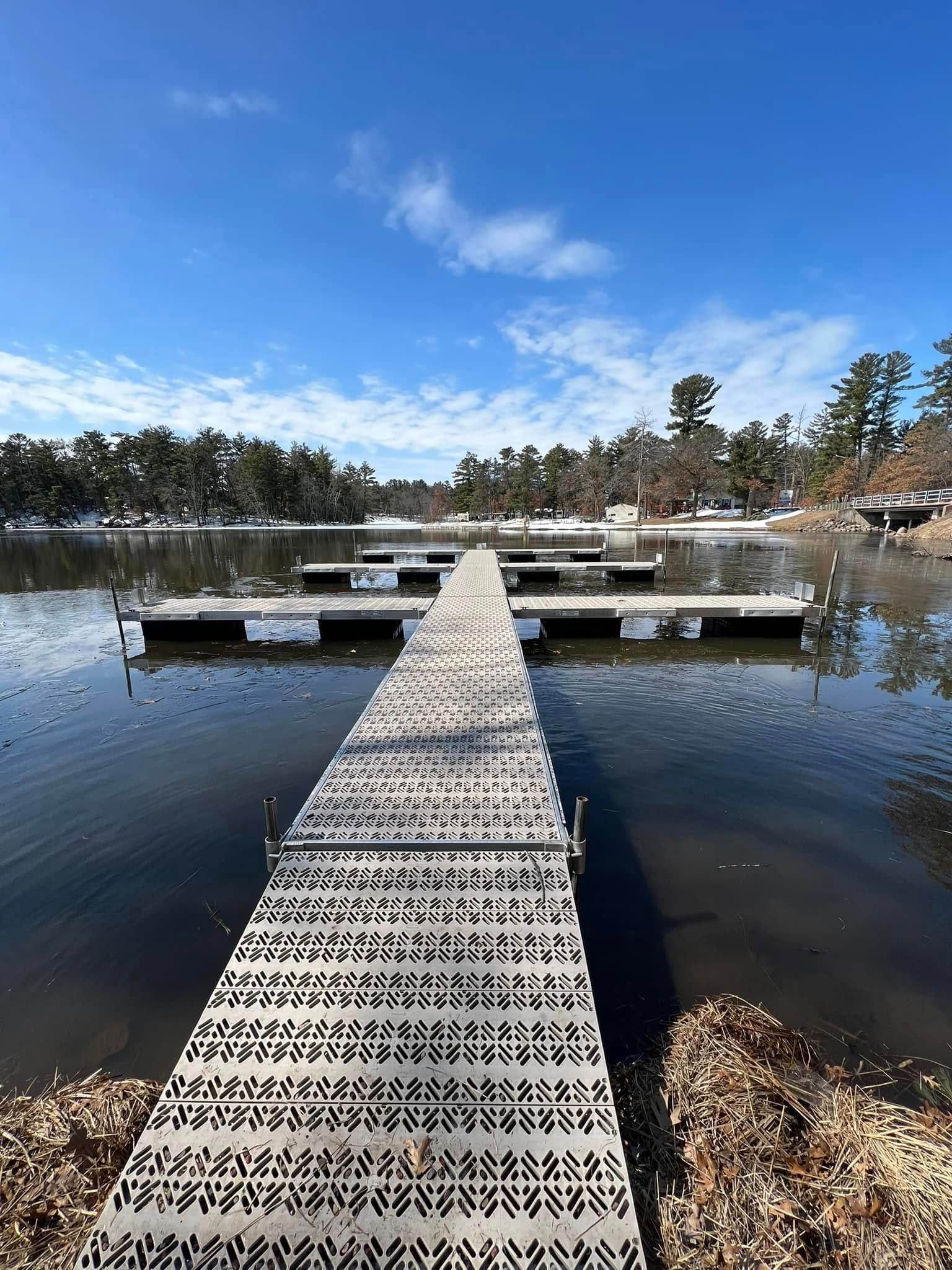 Wooden dock extending into a calm lake under a bright blue sky, with trees along the shore