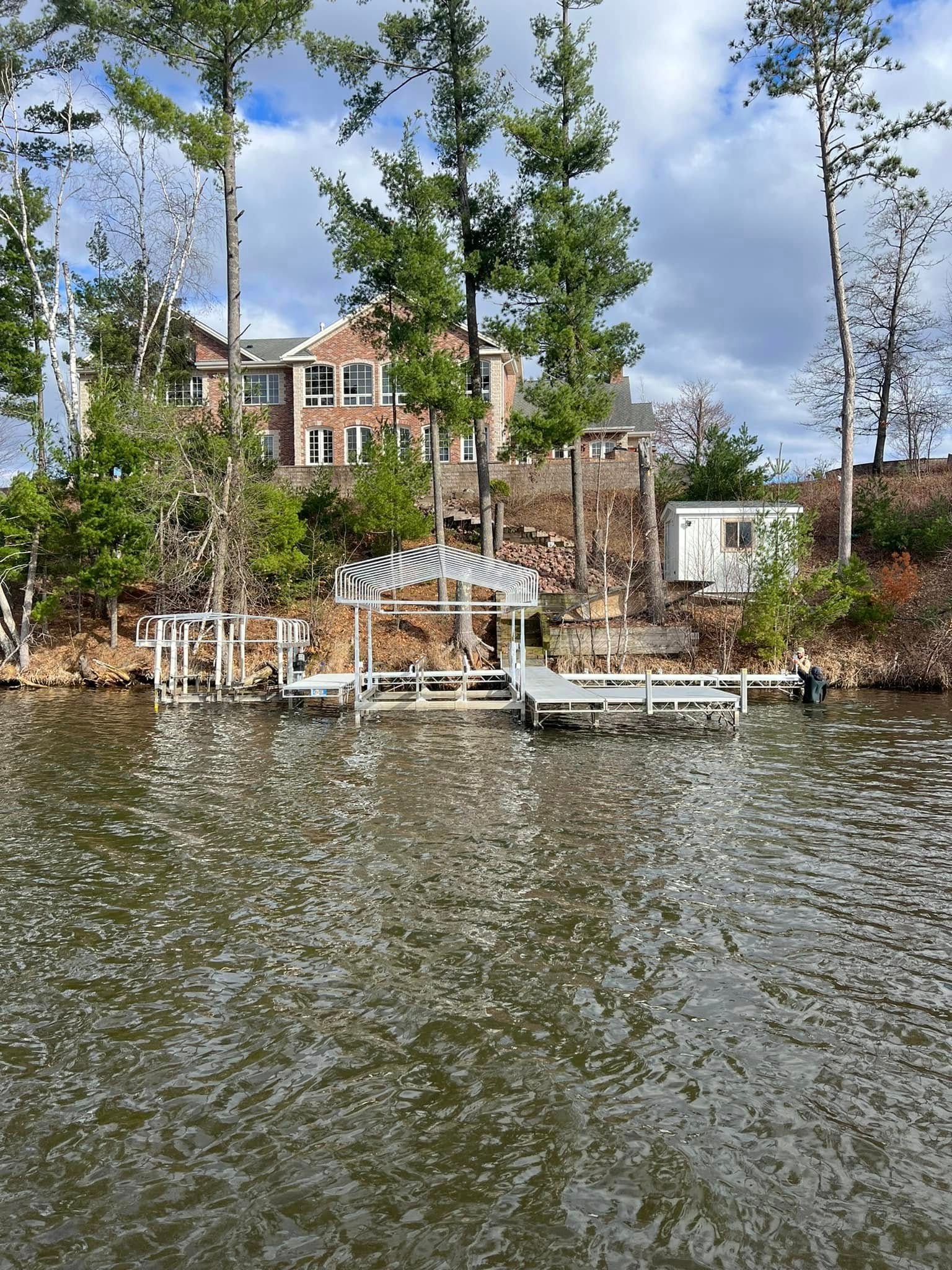 Lakefront house with docks and trees along a calm shoreline under a cloudy sky