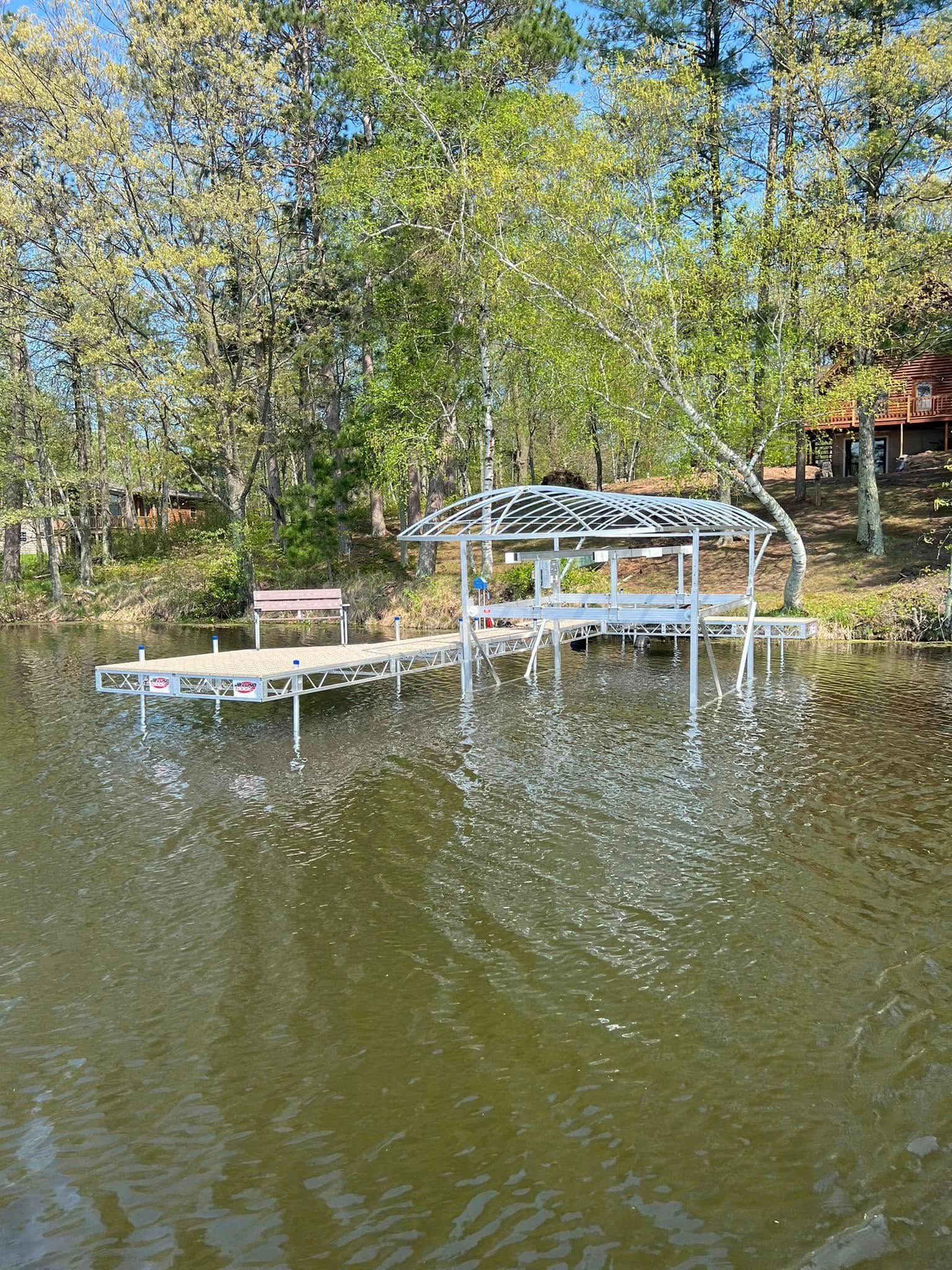 Wooden dock with white canopy over calm lake water, surrounded by leafy trees in autumn sunlight