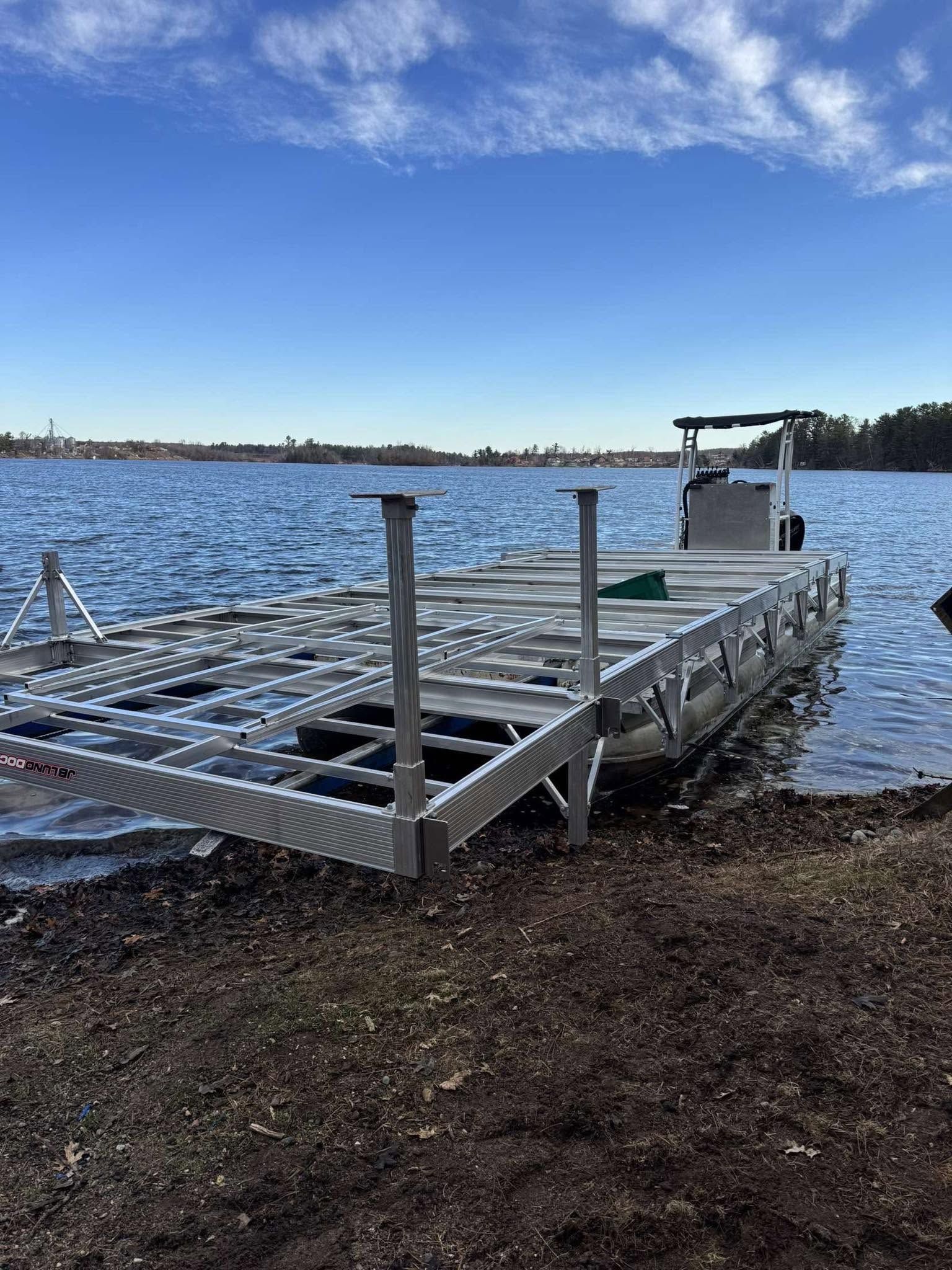 Floating metal dock on a lake under a blue sky, with a grassy shoreline in the foreground.
