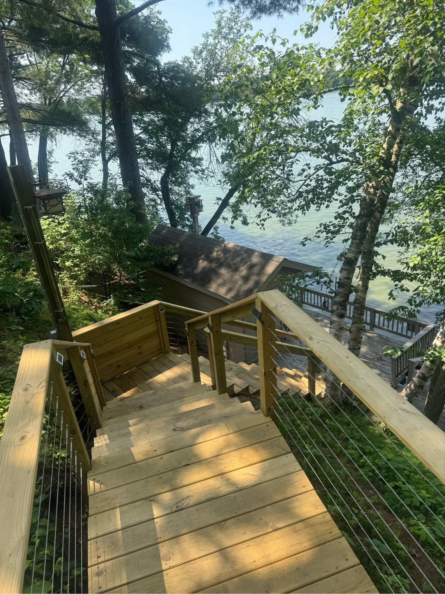 Wooden stairway and deck in a wooded overlook with a lake view beyond.