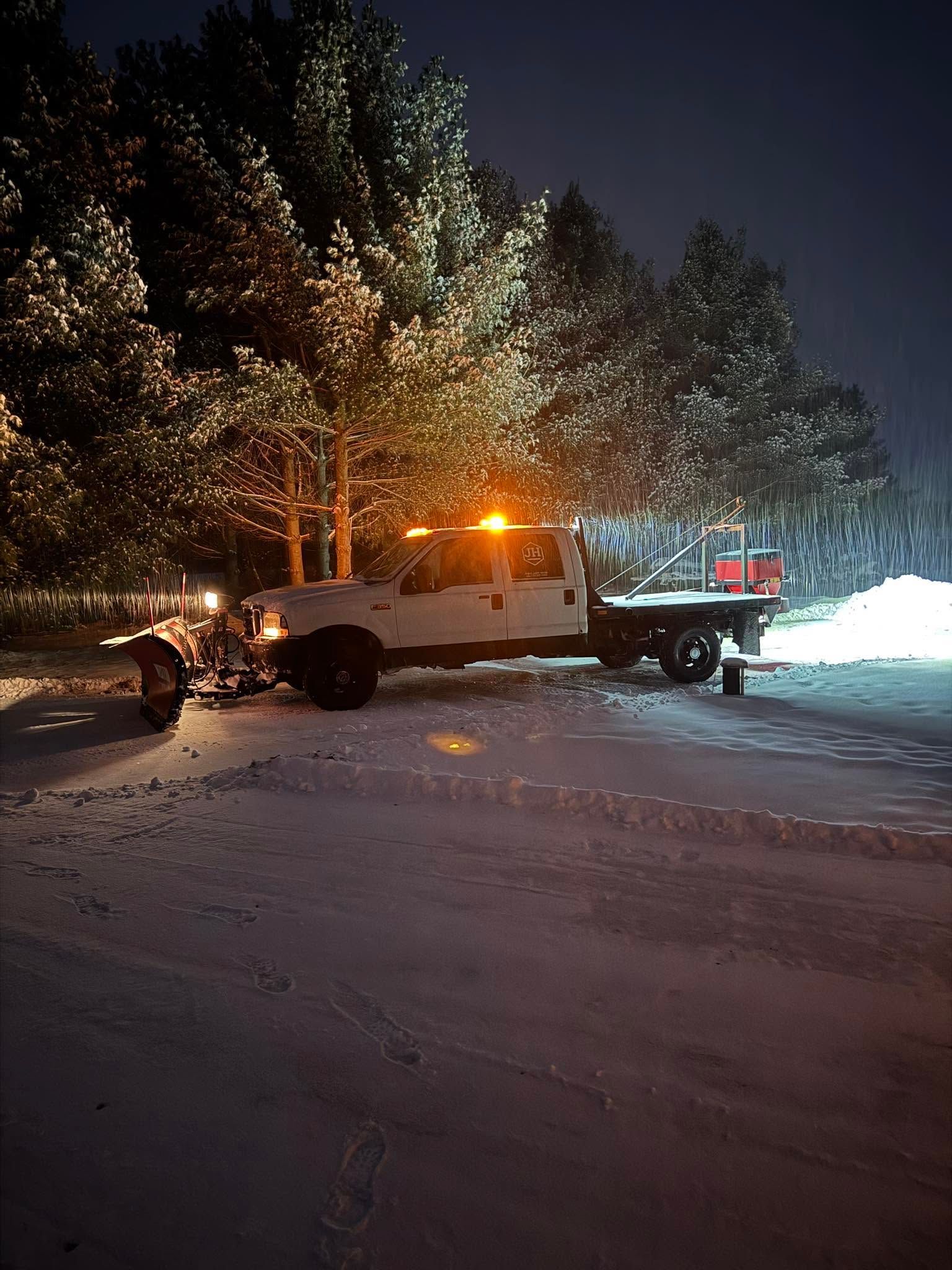 Snowplow truck with flashing amber lights clearing a snowy road at night