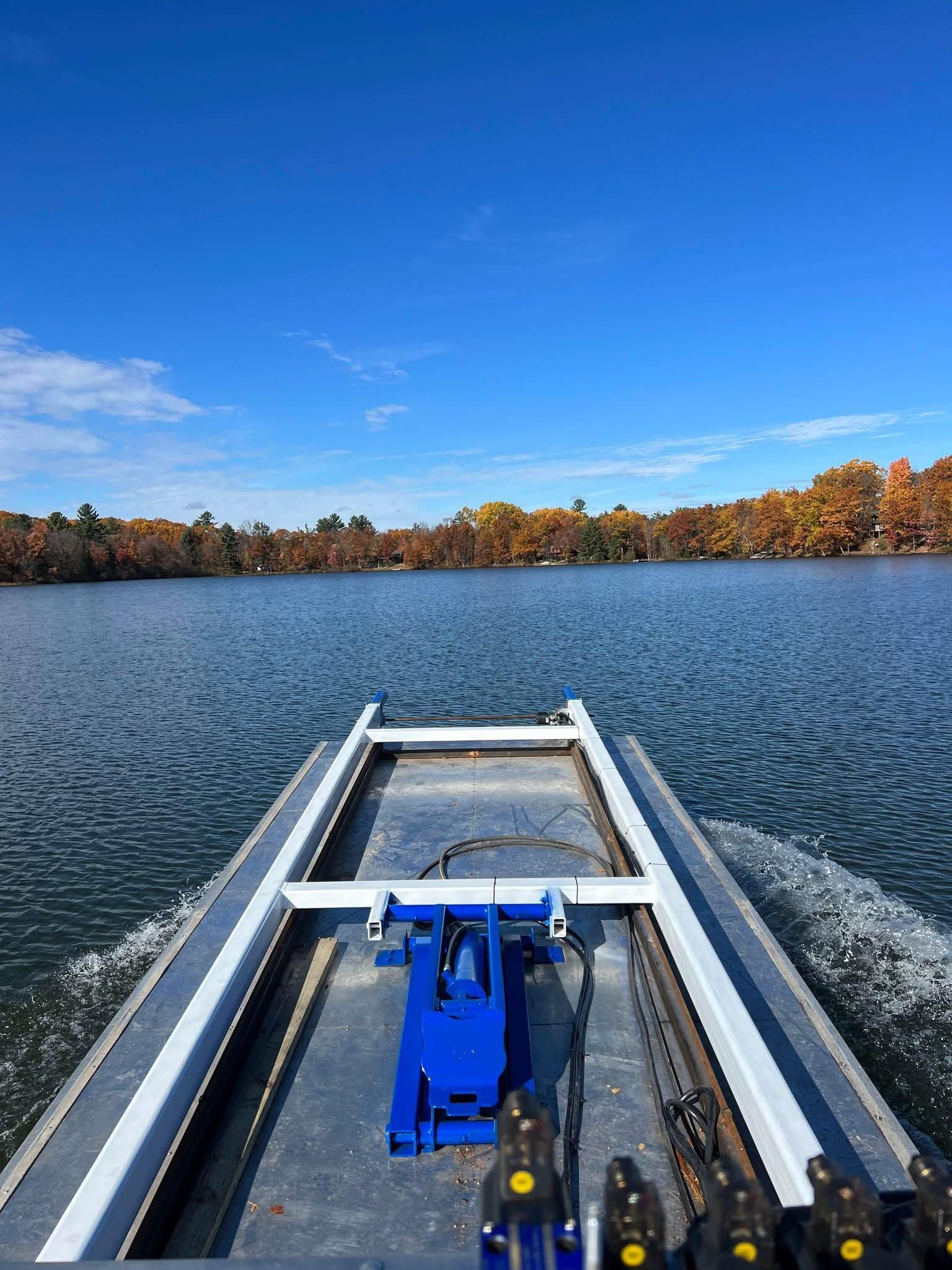 View from a small boat on a lake, with blue equipment in the foreground and autumn trees along the shore.