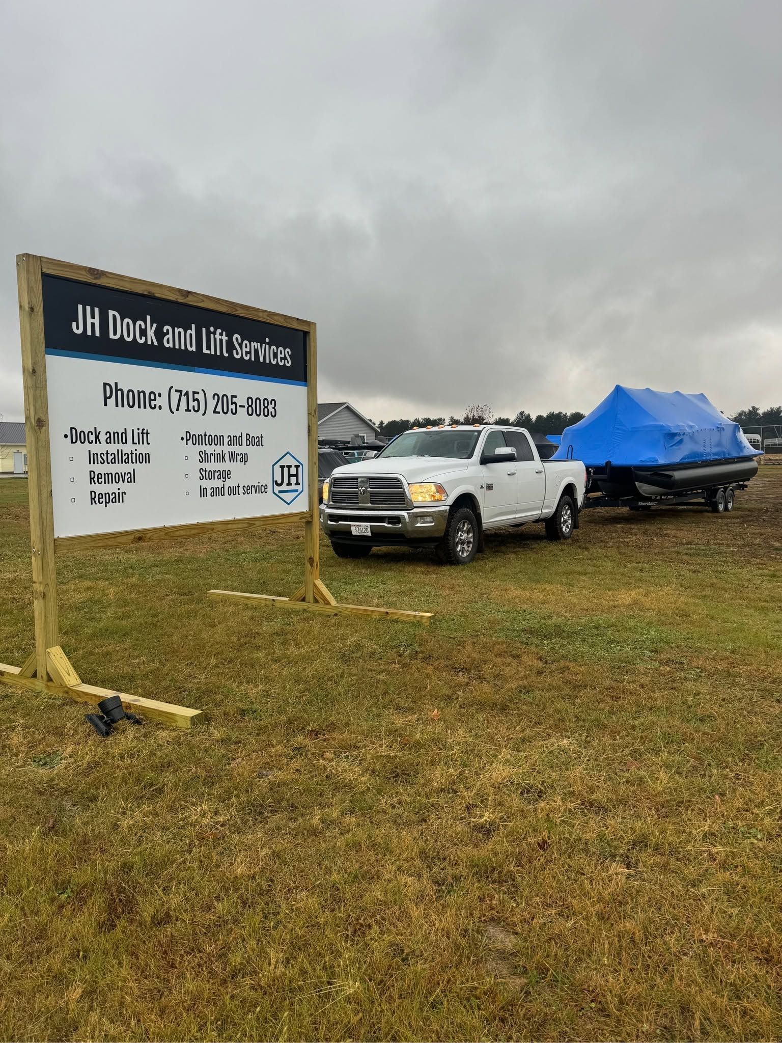 White pickup and blue tarp-covered trailer beside a sign in a rainy grassy field