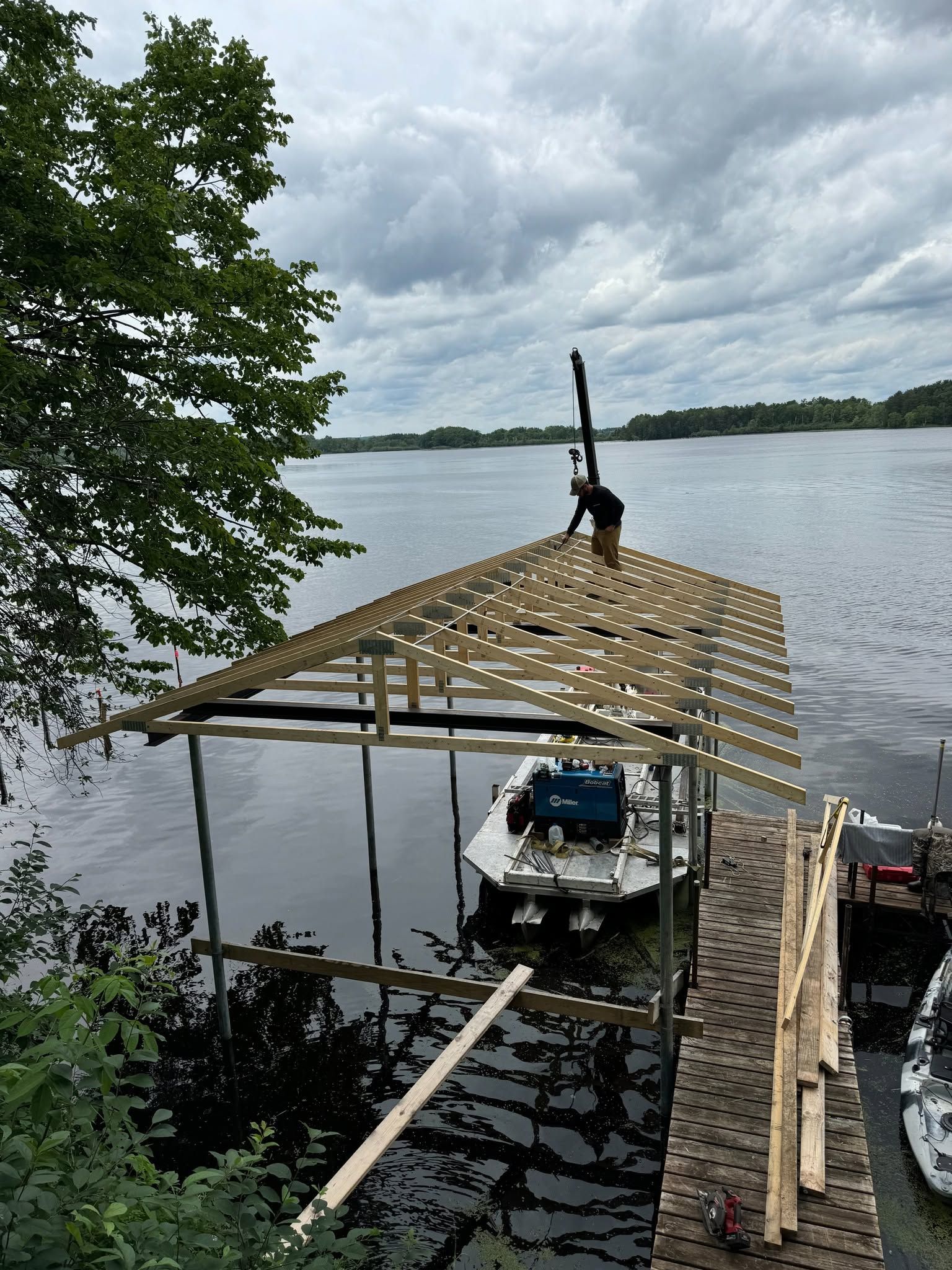 Boat dock under construction beside a lake, with roof trusses and a small boat beneath.