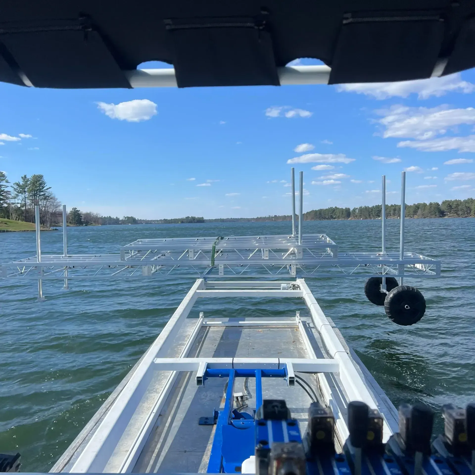 View from a boat bow on a sunny lake, with dock posts and blue water ahead.