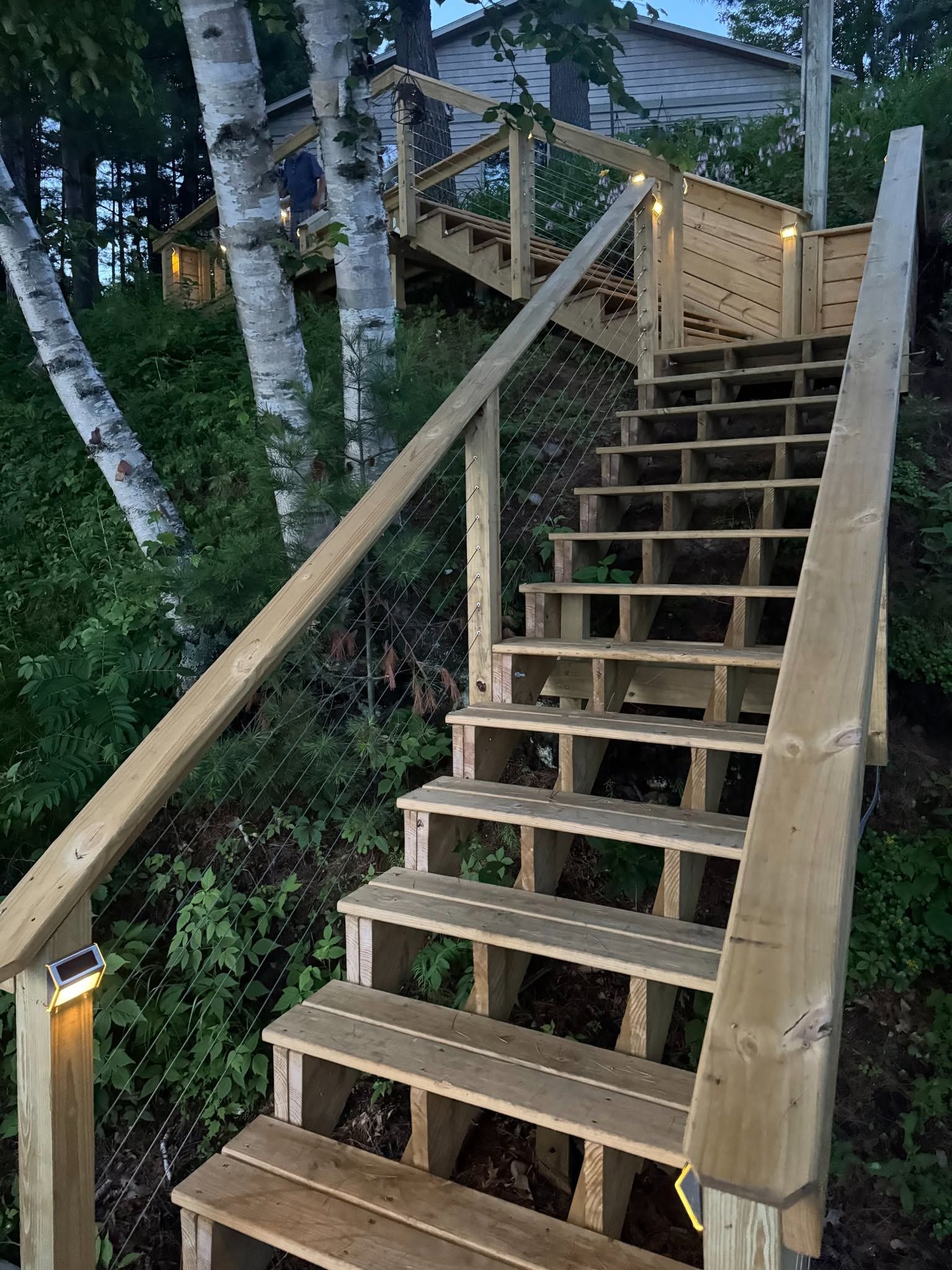 Wooden outdoor staircase with railings leading up a wooded hillside at dusk