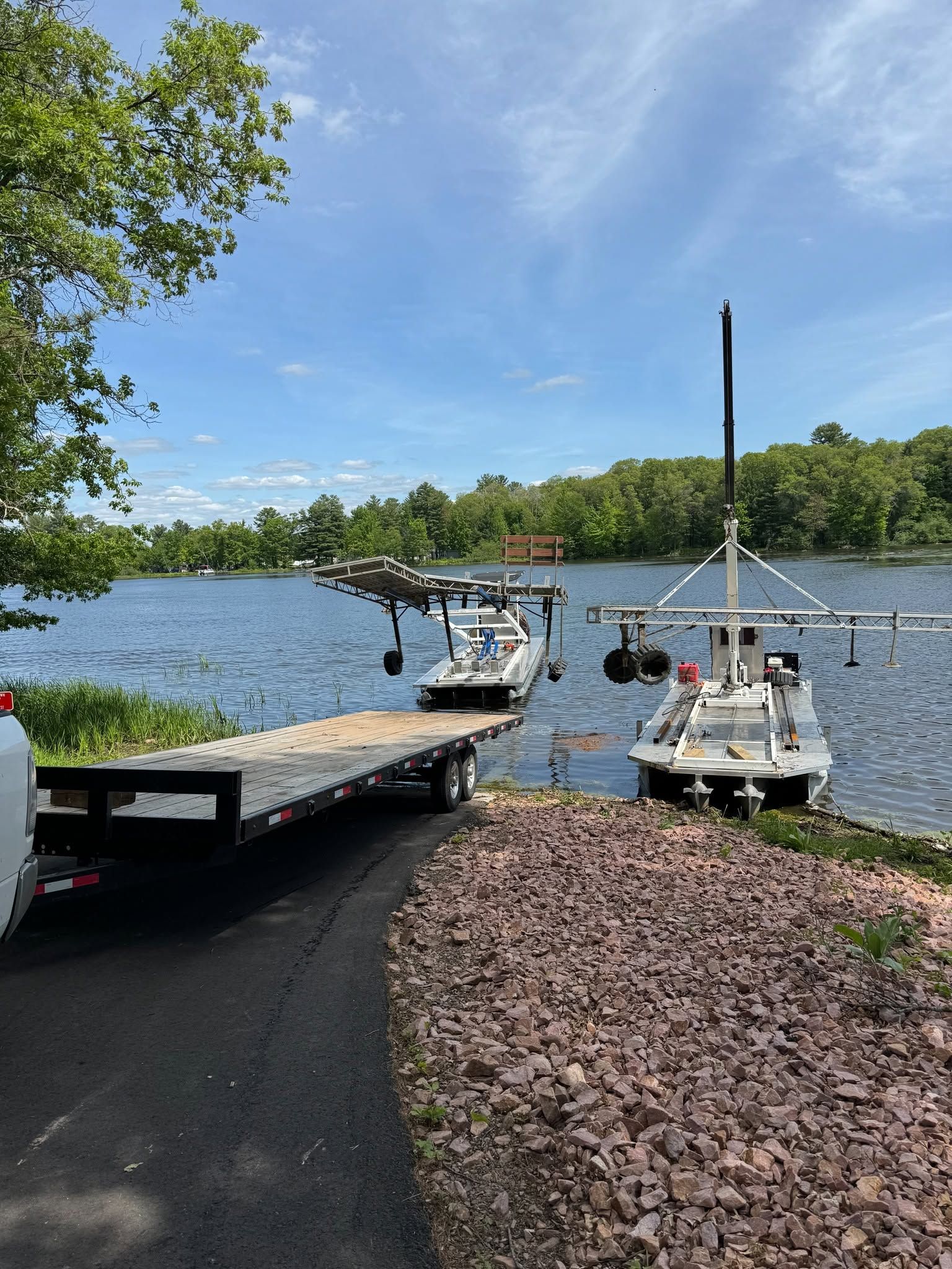 Boat dock on a calm lake with a floating dock, small boats, and tree-lined shore under a blue sky